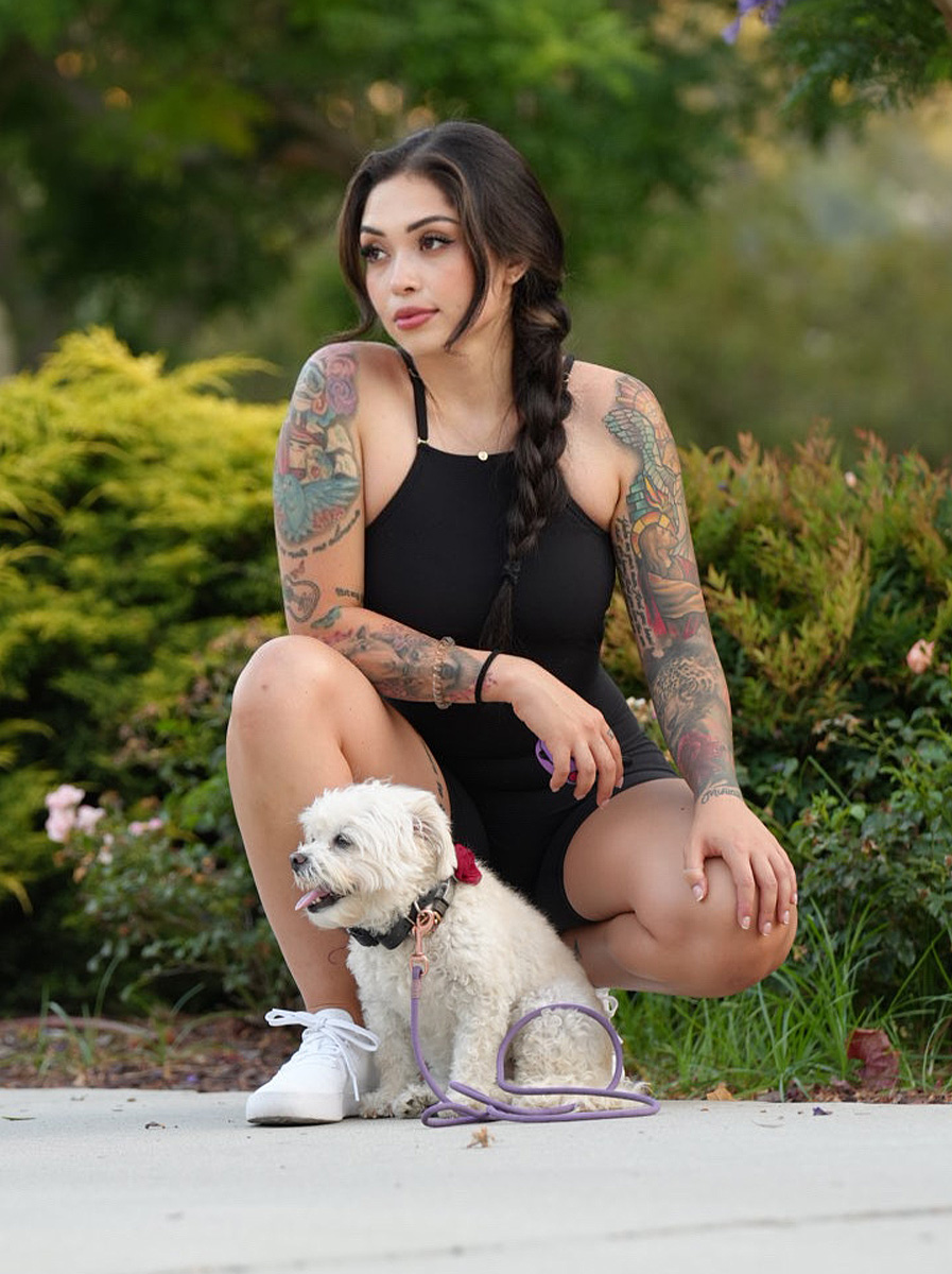 The coach crouches outdoors with her small white dog.
