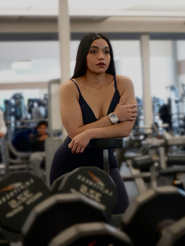 Entrenadora posando en el gimnasio junto al rack de mancuernas.