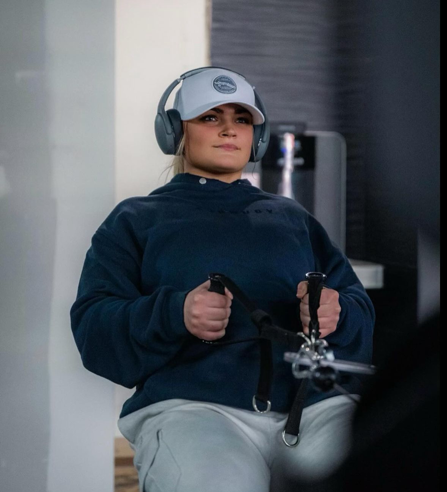 The coach is working out at the gym while listening the musing with her headphone.