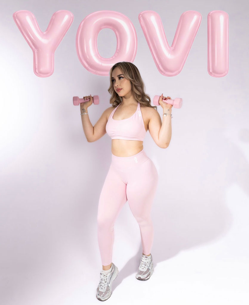 Coach Yovis is posing wearing pink wokrout outfit and holding small dumbells.