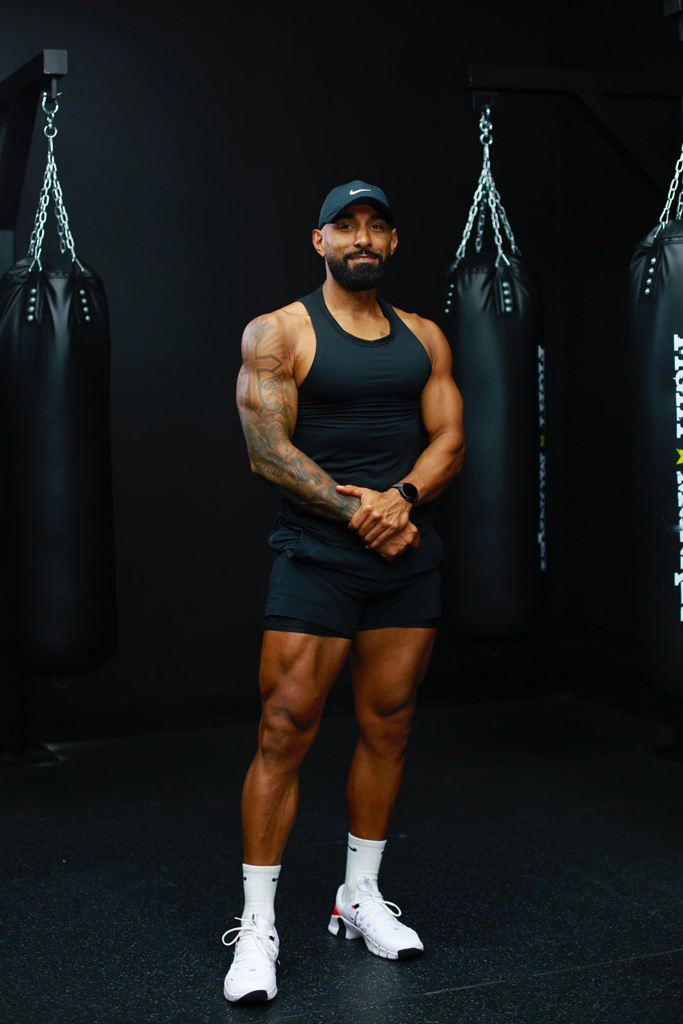 The coach is posing in the gym with black workout outfit.