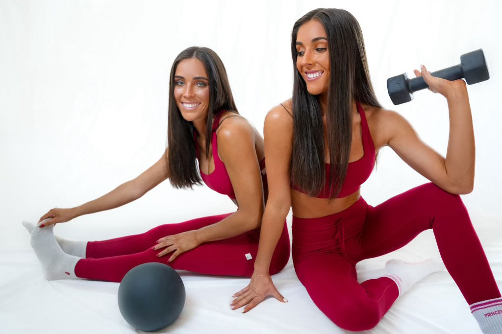 The two coaches posing together with fitness equipment, against a white background.
