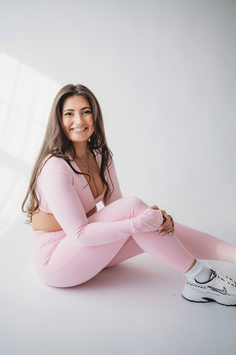 The coach is posing while wearing light pink clothes.