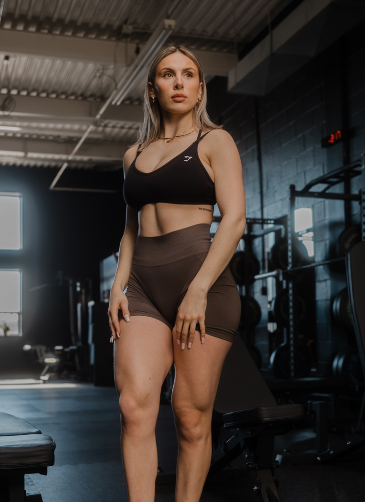 Coach is posing in the gym in a brown workout outfit.